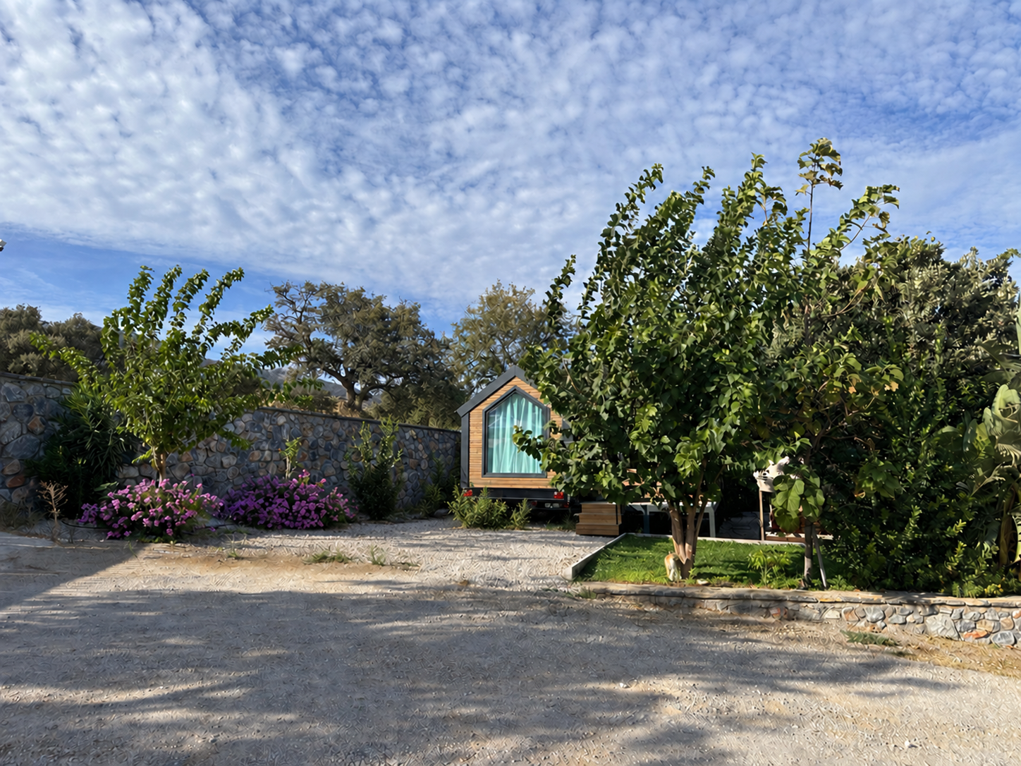 Bitez Efe Camping’de ağaçlar ve taş duvarlarla çevrili tiny house alanı